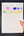 Sheet of watercolor swatches held by a hand with colorful nail polish on a dark surface.