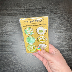 Handmade wax seal stickers in a clear package held by a hand on a gray surface