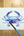 Watercolor painting of a blue crab on white paper with a paintbrush on a wooden surface.