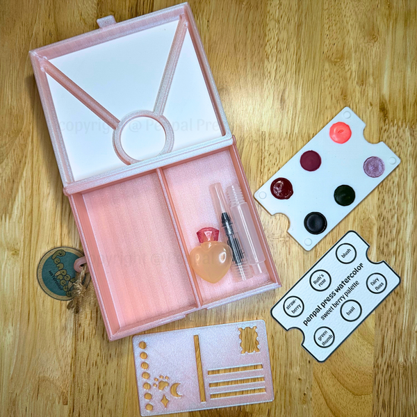 Pink paint box, sweet berry palette, and stencils on a wooden surface.