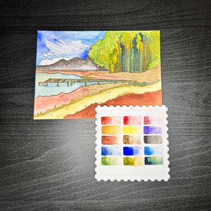 Color swatch card with watercolor landscape painting on a dark wooden surface