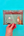 Hand holding a card with a cat sitting under a desk against a green background