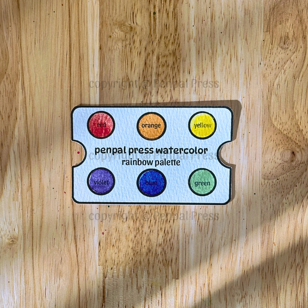 Penpal Press watercolor rainbow palette on a wooden surface