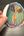 Hand holding a colorful sticker with artistic depiction of hands with a mirror finish on a dark surface