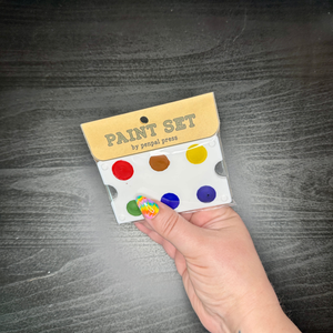 Hand holding a paint set with color samples against a dark wooden surface