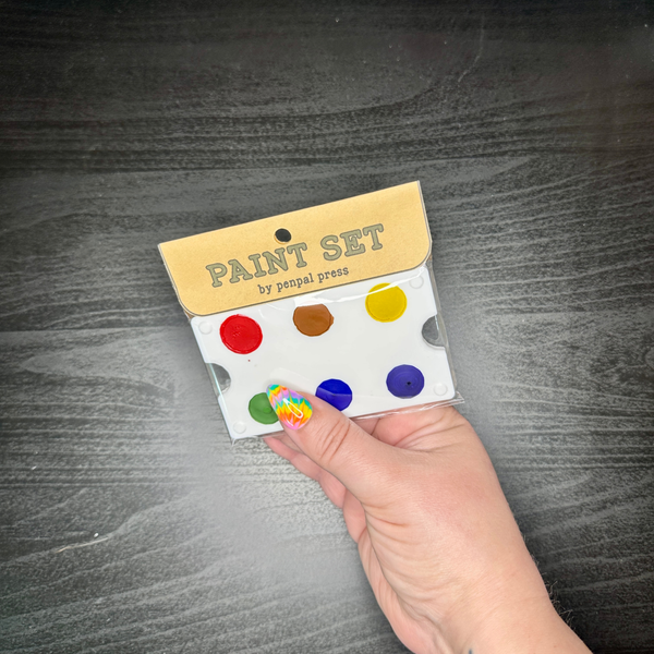 Hand holding a paint set with color samples against a dark wooden surface