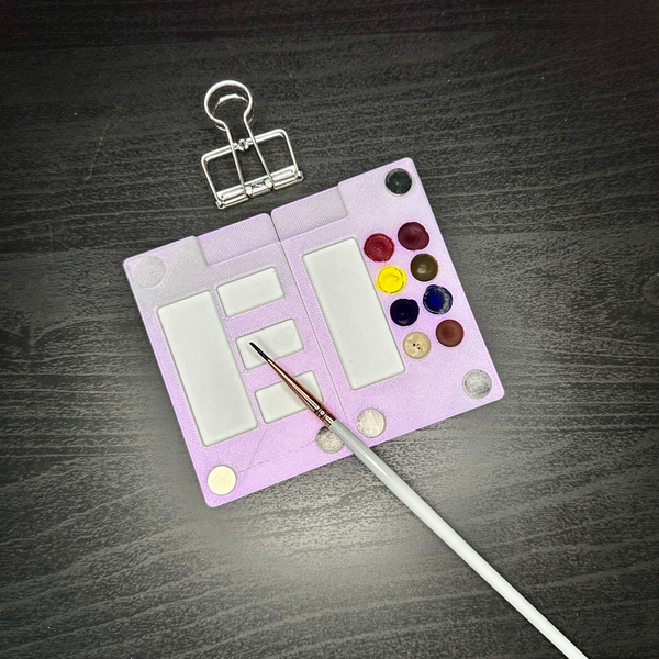 Small paint palette with watercolors and a brush on a dark wooden surface