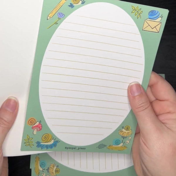 Hand holding a green note with decorative snail border and lined paper