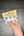 Hand holding a small paint set with colorful dots against a dark wooden surface