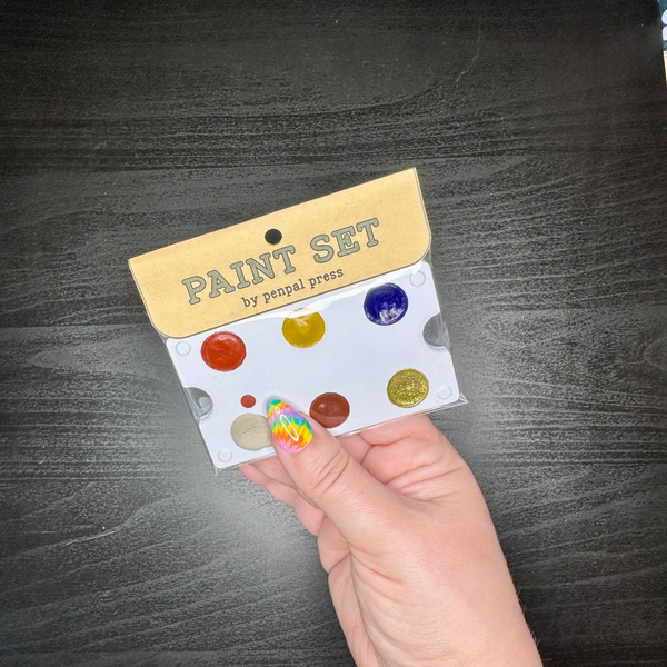 Hand holding a paint set with colorful dots on a dark wooden surface