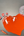 Three small watercolor pans of different sizes  filled with orange-red paint, a metal spatula with wet watercolor paint, a heart shaped area of wet venetian red paint on a glass slab, with a glass muller at the top right.