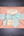 A square package wrapped in textured kraft paper, tied with a frayed sage green ribbon and bow, with a vintage-style paper label in the center, photographed from above on a dark wood background.