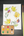 A fall leaf design painted with yellow, orange, purple, red, and green watercolor, on a dark wood background with a set of dots of watercolor and yellow handled paintbrush.