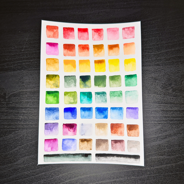 Sheet of watercolor swatches on a dark wooden surface.