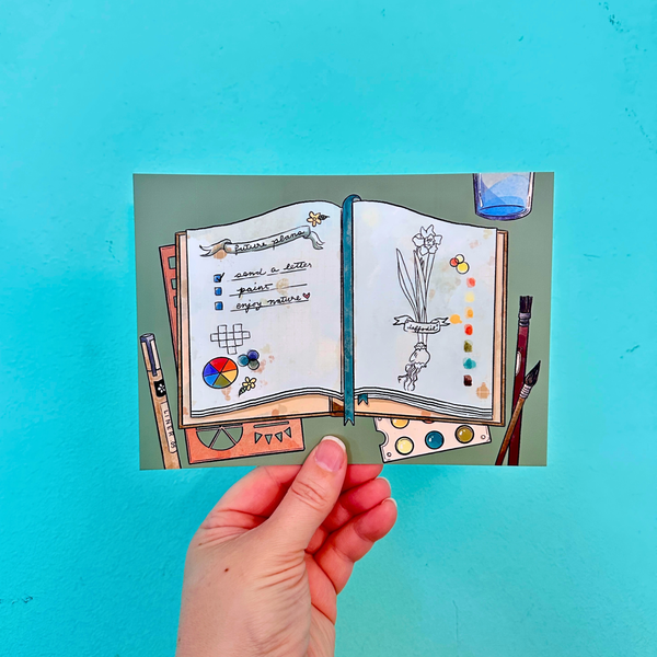 Hand holding a small open book with illustrations on a teal background