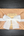 A square kraft-paper wrapped package tied with a white frayed ribbon and a small paper label, photographed from above on a dark wood surface.