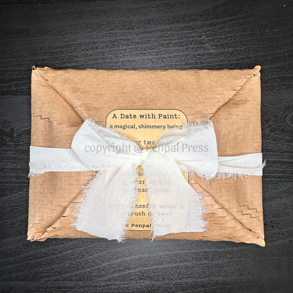 A square kraft-paper wrapped package tied with a white frayed ribbon and a small paper label, photographed from above on a dark wood surface.