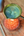 small pink candle melting green wax in a metal spoon, on a wooden surface with a spoon and other items.