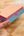 Colorful watercolor paint box with 'Penpal Press Watercolor' branding held by a hand on a wooden surface.