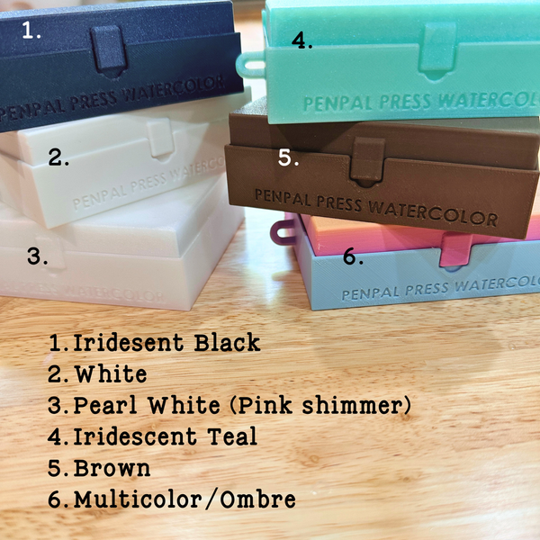 Stacks of Penpal Press Watercolor container boxes in various colors on a wooden surface.
