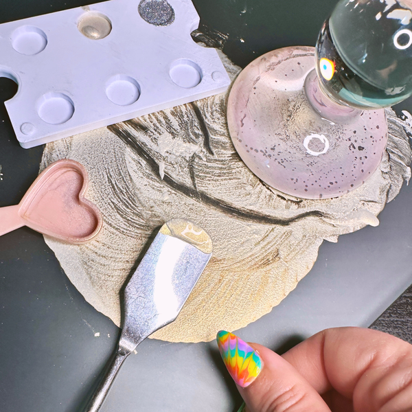 Close up of a glass slab with palette knife, heart shaped measuring spoon, glass muller, and half empty paint pan set.
