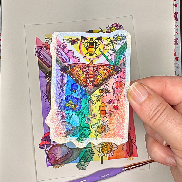 Colorful rainbow flag sticker with intricate designs held by a hand on a light background