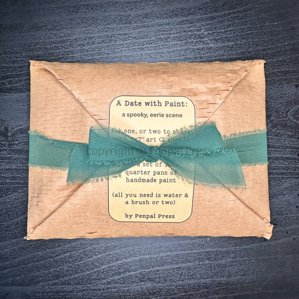 A handmade paper envelope-style package wrapped with a deep green ribbon, featuring a vintage-style label that reads 'A Date with Paint: a spooky, eerie scene' and 'by Penpal Press,' placed on a dark wood background.
