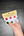Hand holding a small paint set with colorful dots on a dark wooden surface
