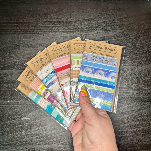 Hand holding a collection of Penpal Press washi tape samples on a wooden surface